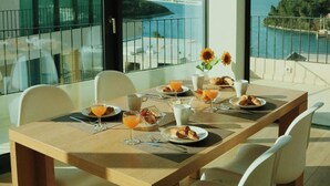 A dining area with a table set for breakfast, overlooking a scenic view of a body of water and hills. - White Cloud Apartments (Korcula)