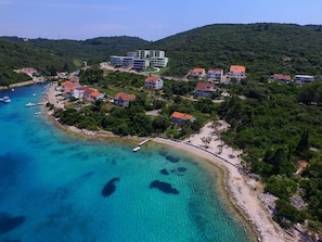 Luftaufnahme einer Küstenstadt mit Häusern, einem Strand und klarem, blauem Wasser.