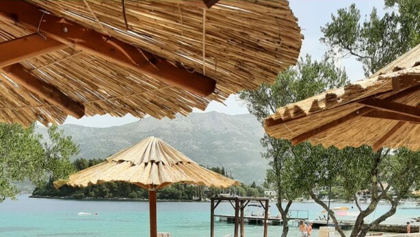 A beachside lounge area with wooden loungers and thatched umbrellas, overlooking a calm sea and distant mountains. - White Cloud Apartments (Korcula)