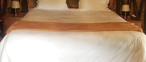 Una cama con cabecera de madera, dos mesitas de noche con lámparas y un dosel colgante.