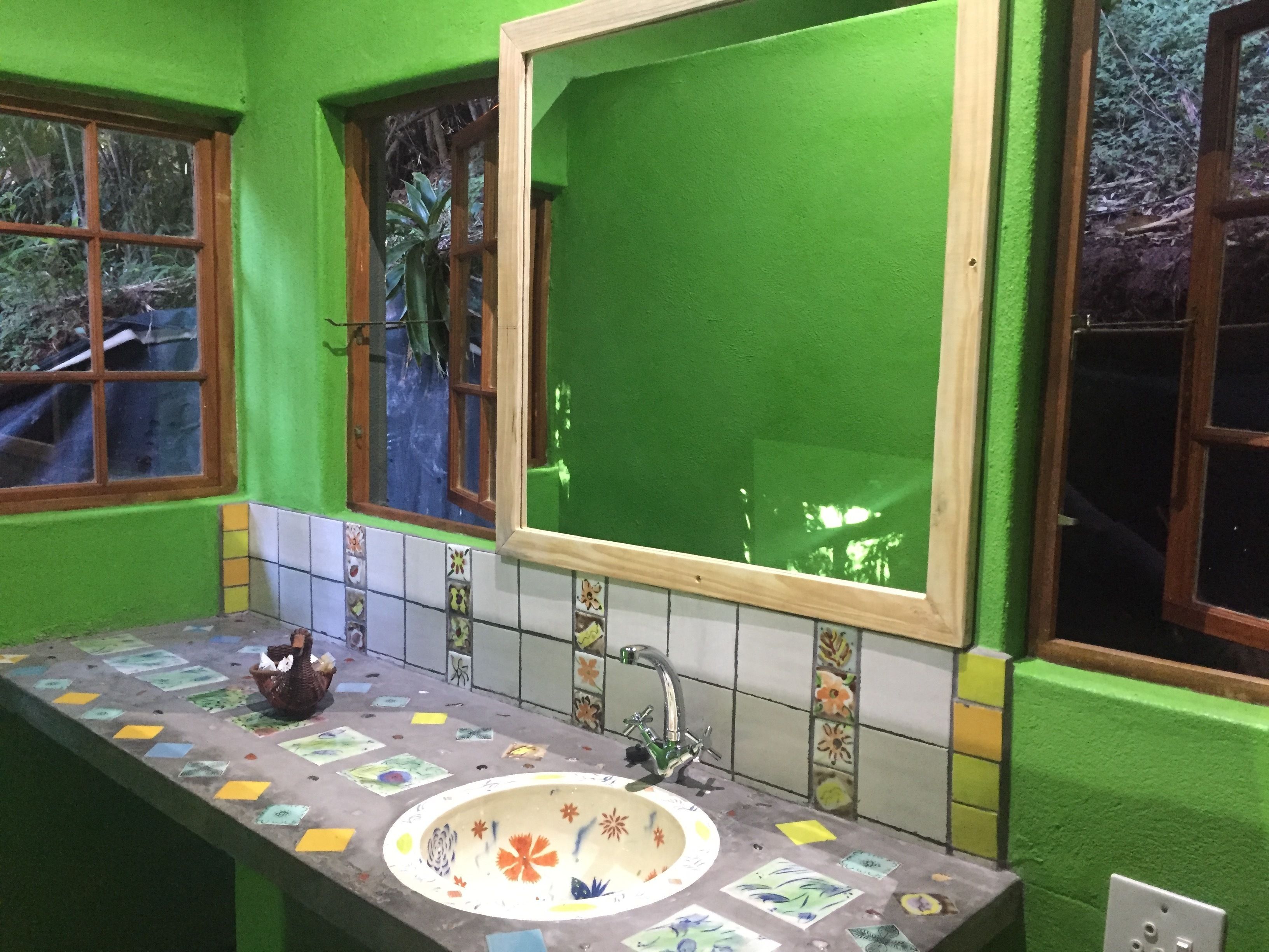 Un baño con paredes verdes, un lavabo con azulejos y una ventana con vistas a árboles.