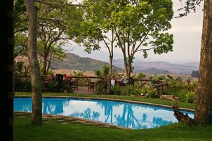 Un área de piscina con cubierta de madera, rodeada de árboles y vistas a colinas distantes.