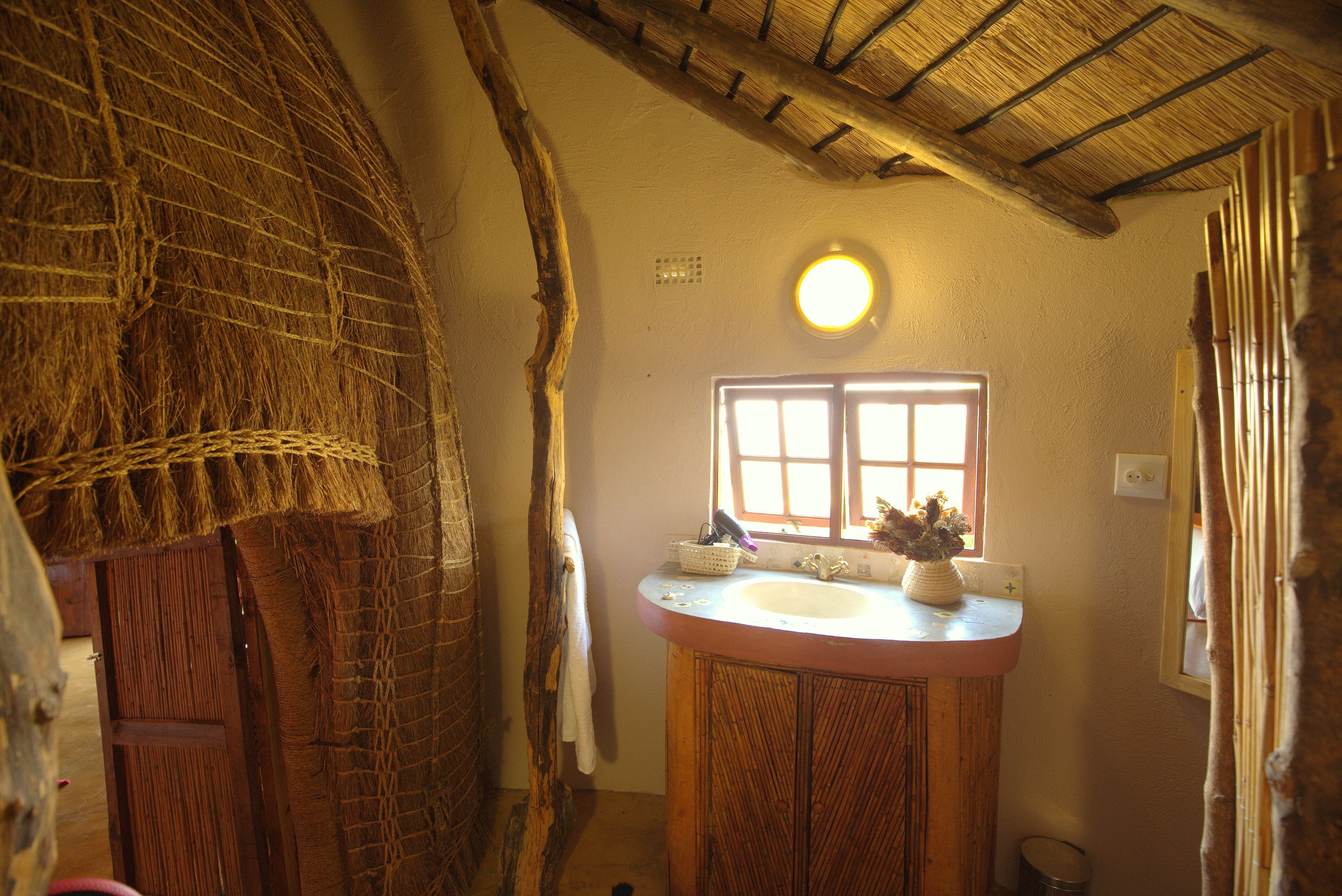 A rustic bathroom with a wooden vanity, a window with natural light, and a thatched ceiling.