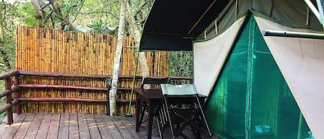 A wooden deck with a table and chairs, a bamboo fence, and a tent with a green mesh side.