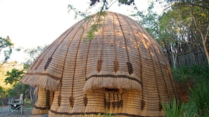 A thatched dome structure with a circular entrance, surrounded by greenery and trees. - Phophonyane Falls Ecolodge (Piggs Peak)