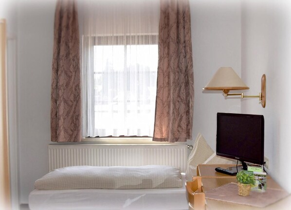 Habitación de hotel con cama, escritorio con computadora, lámpara y ventana con cortinas.