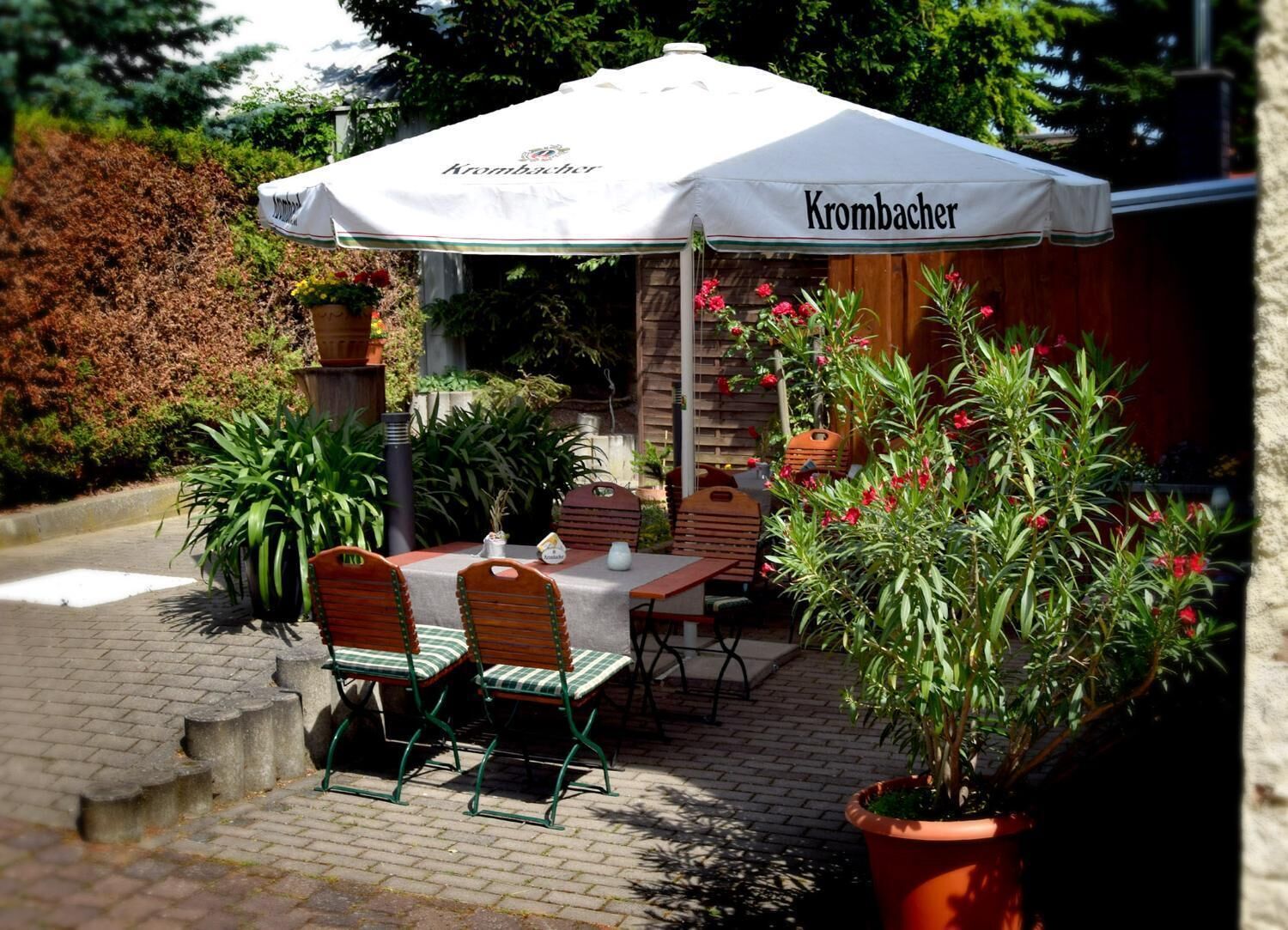 An outdoor patio with a table and chairs under a white umbrella labeled "Krombacher."
