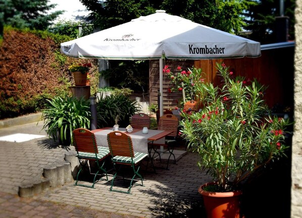 An outdoor patio with a table and chairs under a white umbrella labeled "Krombacher." - Landhotel Stadt Nuernberg (Ahlsdorf)