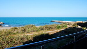 A coastal view with a clear sky, a sandy beach, and a rocky breakwater.