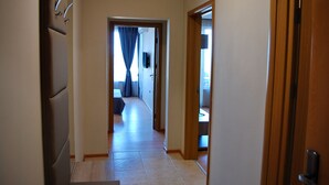 A hallway with a door on the right, a door on the left, and a window with curtains in the center.