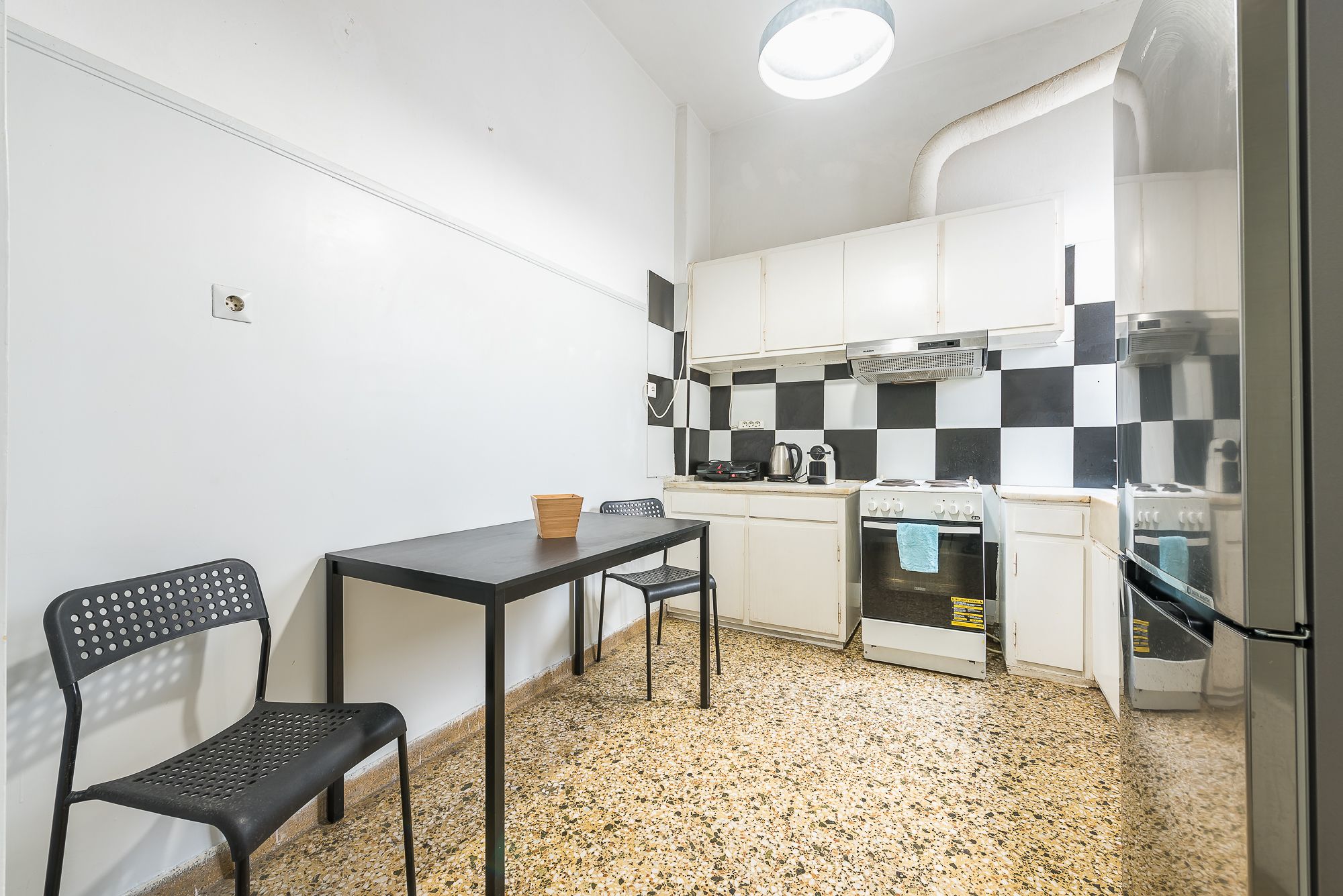 Une cuisine compacte avec un crédence à carreaux, une petite table à manger, deux chaises et un réfrigérateur.