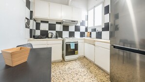 Une cuisine compacte avec des meubles blancs, un crédence à carreaux noirs et blancs, un réfrigérateur en acier inoxydable, une cuisinière et un four à micro-ondes.