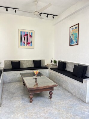 Una sala moderna con una mesa de centro de vidrio, un ventilador de techo y dos obras de arte colgadas en la pared.
