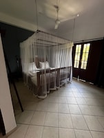 A room with a bed under a canopy, a ceiling fan, and a view of the outdoors through a window.