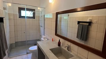 Un baño con ducha, inodoro, lavabo y un espejo grande.