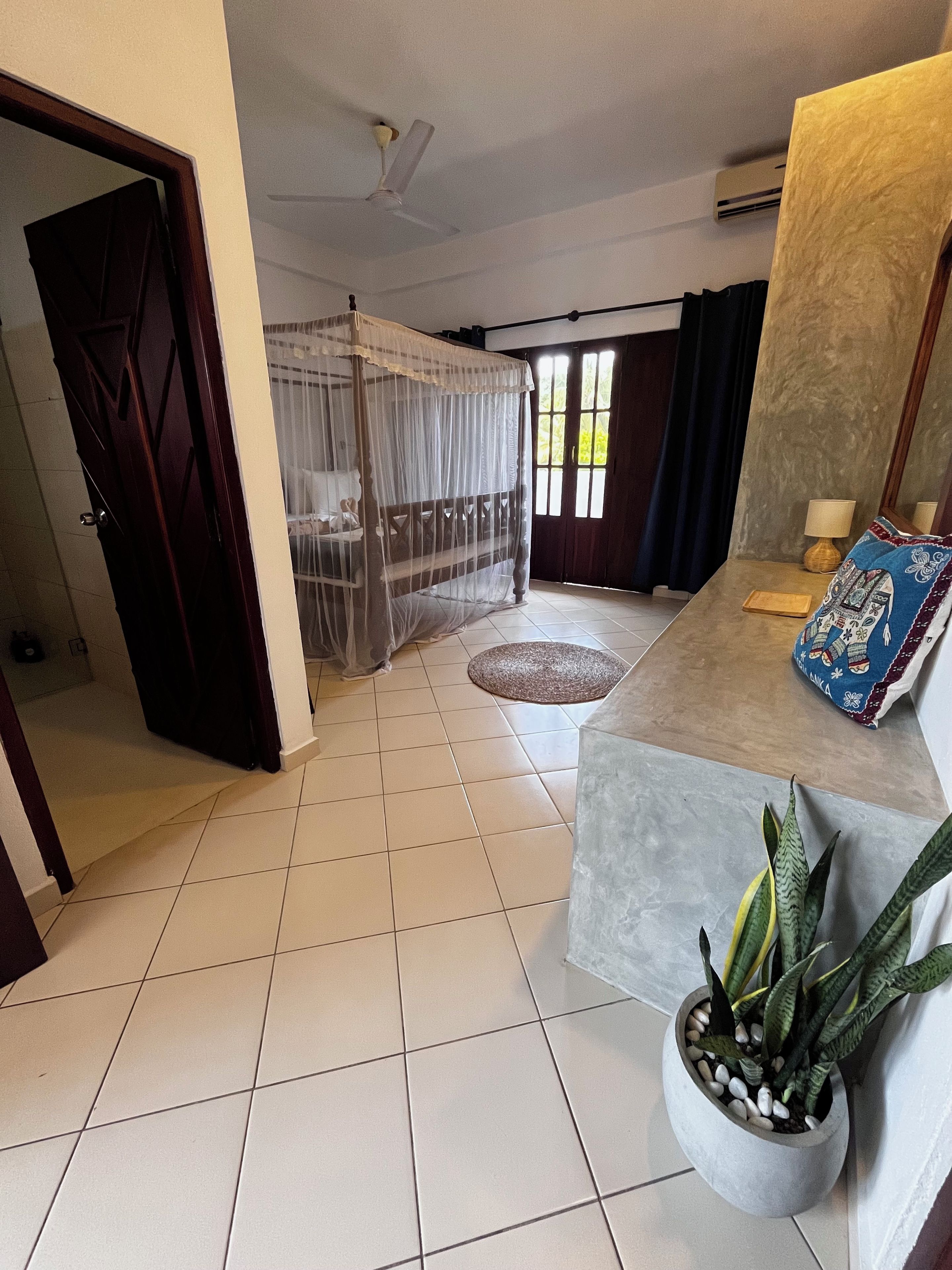 A room with a bed, a ceiling fan, a potted plant, and a window with curtains.