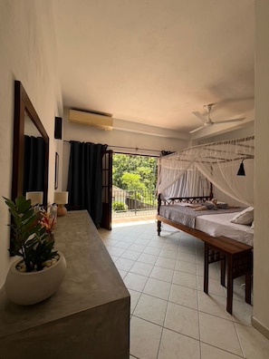 A bedroom with a bed, a bedside table, a mirror, a ceiling fan, and a view of the outdoors. - Unawatuna Nor Lanka Hotel (Unawatuna)