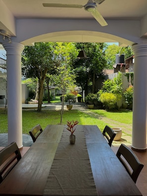 An outdoor patio with a long table and chairs, surrounded by greenery and a clear view of the backyard. - Unawatuna Nor Lanka Hotel (Unawatuna)
