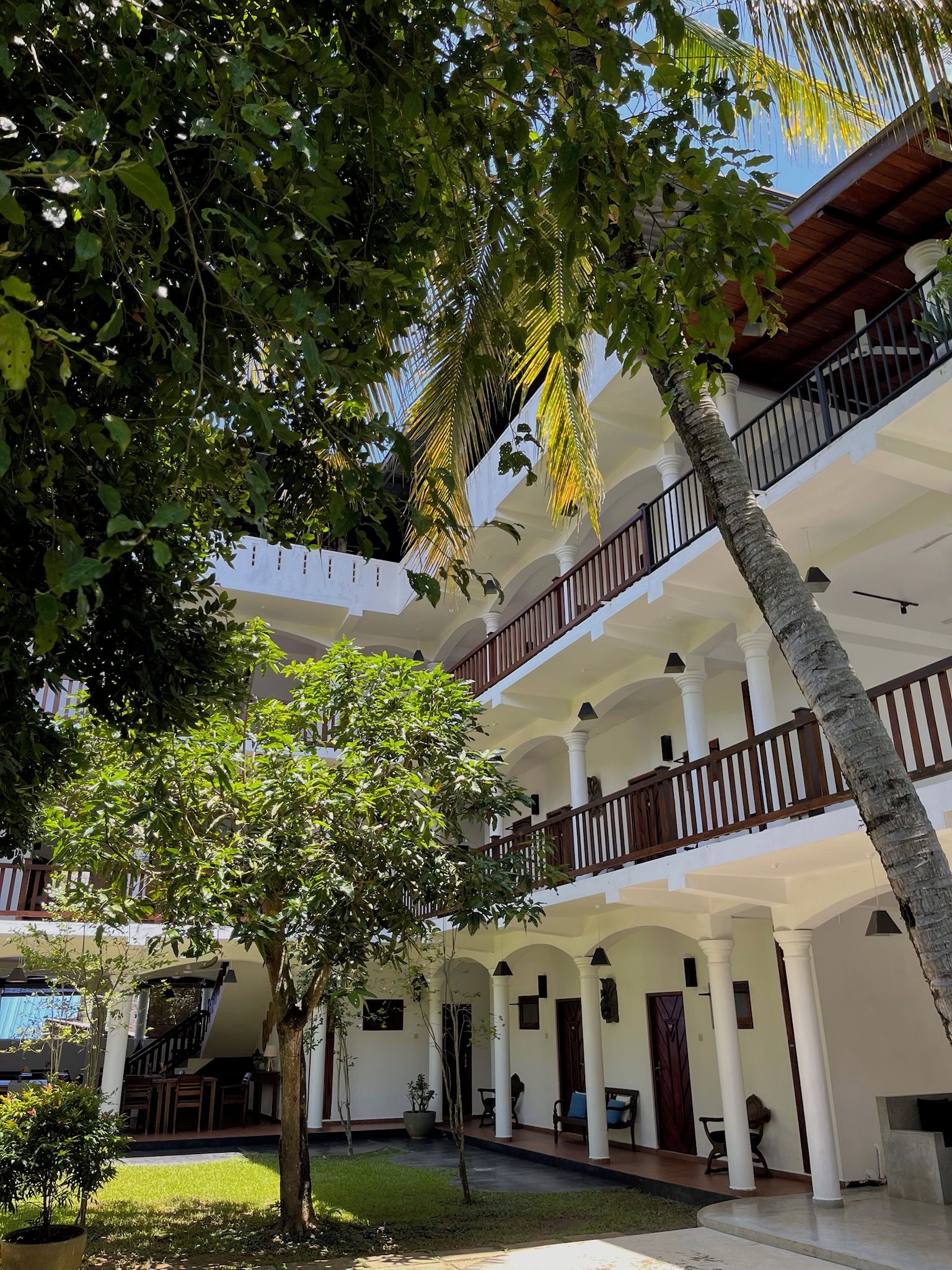 A multi-story building with a courtyard, featuring balconies, columns, and a palm tree.