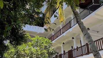 A multi-story building with a courtyard, featuring balconies, columns, and a palm tree.