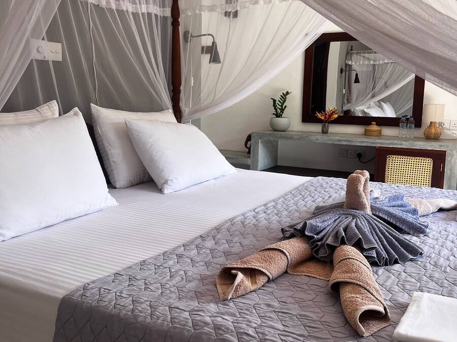 Una cama con dosel, almohadas, colcha acolchada y toallas.