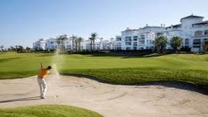 Ein Golfplatz mit einem Sandbunker und einem Gebäude im Hintergrund.