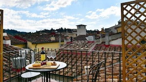 Une terrasse sur le toit avec une table dressée pour un repas, comprenant du fromage, des noix et des verres à vin.
