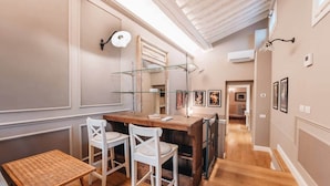 Un couloir avec un plancher en bois, une table en verre et des chaises blanches.