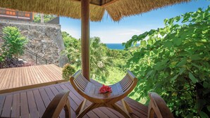 A wooden deck with a bench, a thatched roof, and a view of the ocean.