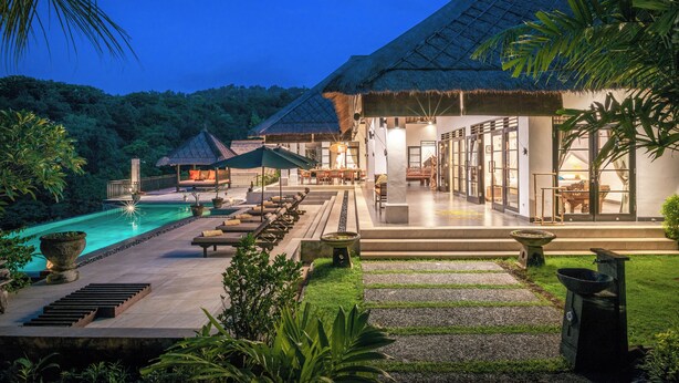 A resort with a swimming pool, lounge chairs, and a thatched-roof building.