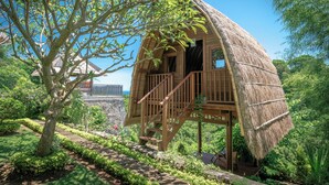 A treehouse with a thatched roof, wooden staircase, and a view of the surrounding greenery.