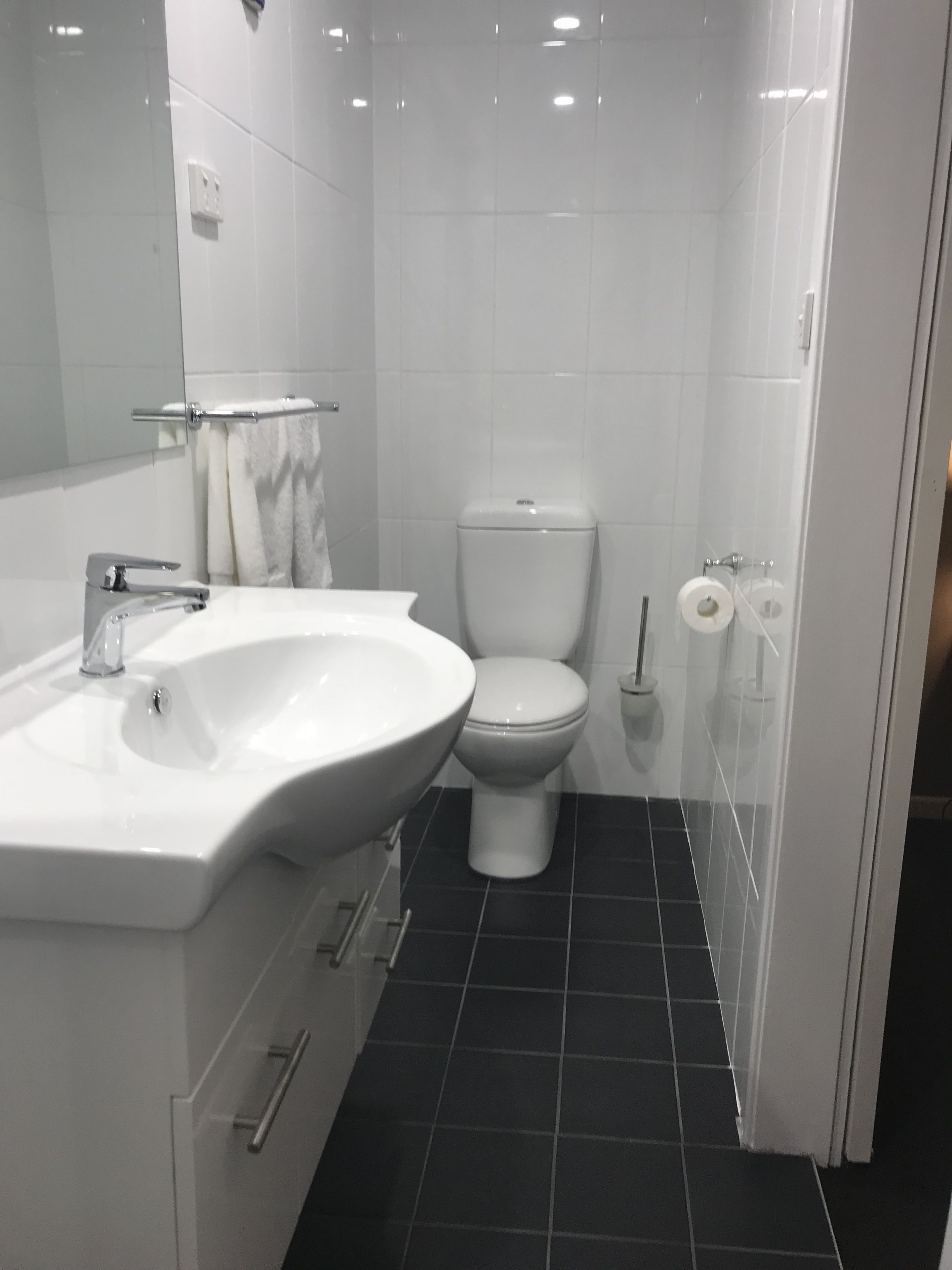 Een badkamer met een wit wastafelmeubel, toilet en een douchecabine van glas.