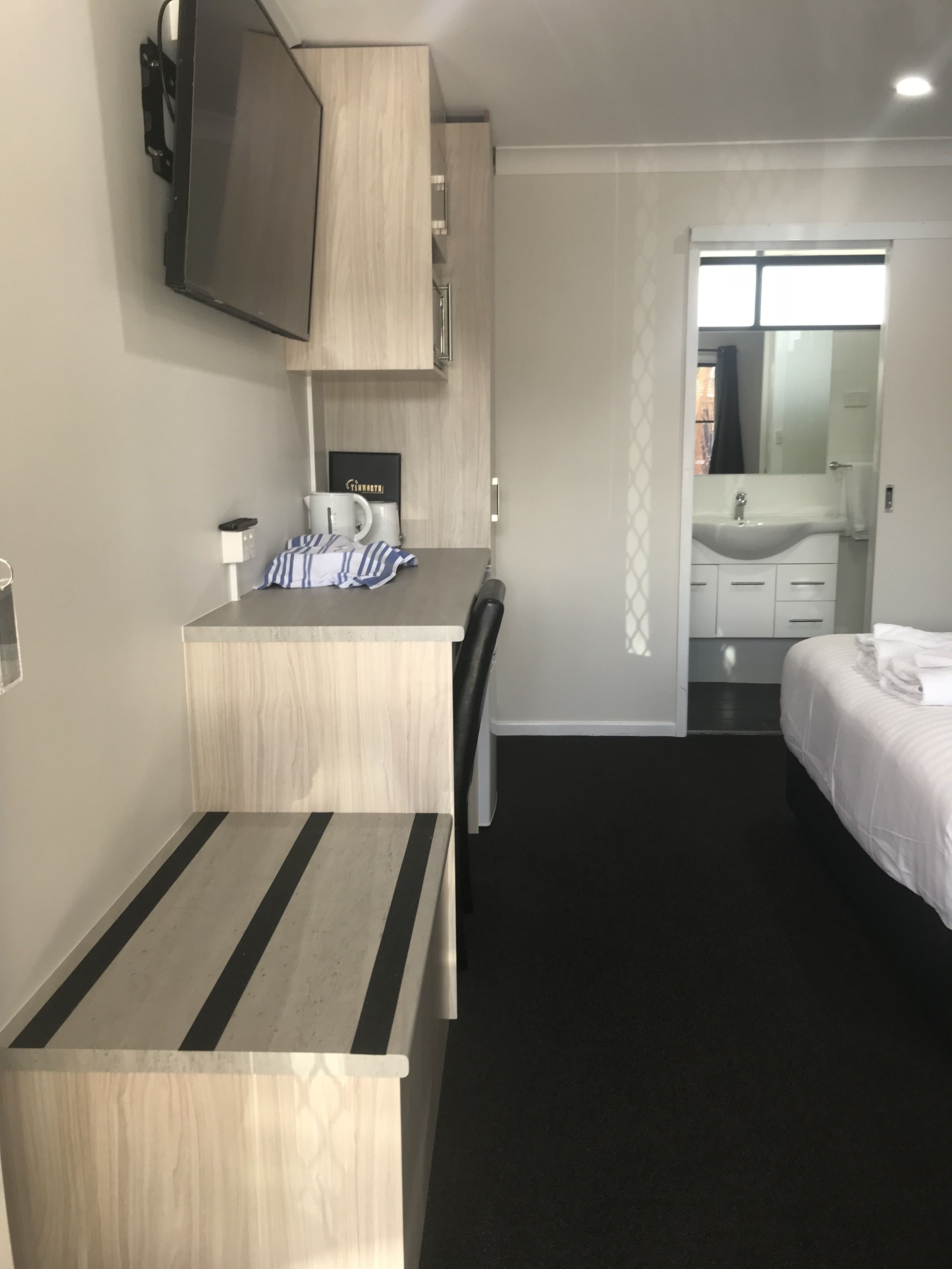 Una habitación de hotel con cama, escritorio, silla, televisión, lavamanos y espejo.