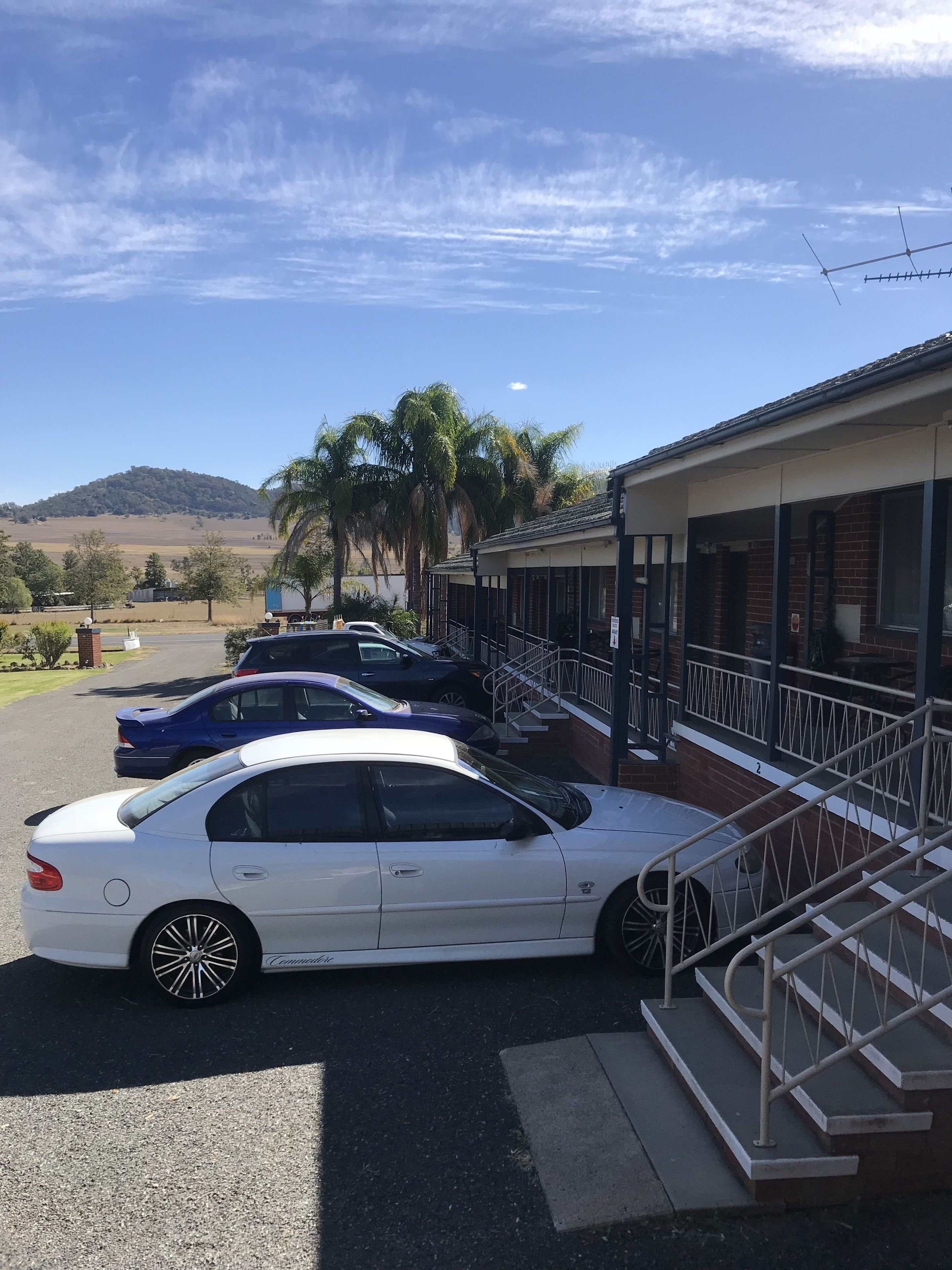 Un estacionamiento con varios autos, un edificio de ladrillo y una colina al fondo.