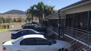 Un estacionamiento con varios autos, un edificio de ladrillo y una colina al fondo.