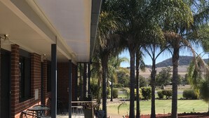 Un espacio al aire libre techado con patio, asientos y vistas a un jardín ajardinado con palmeras.