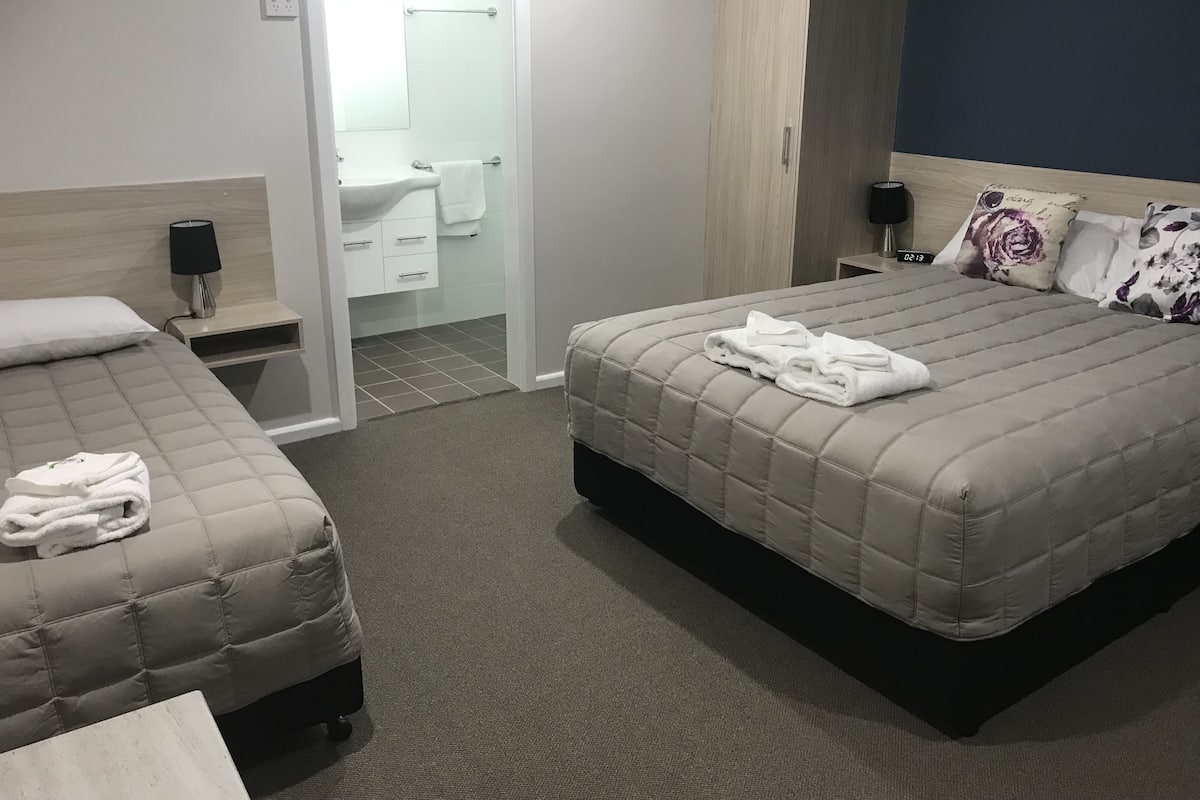 A hotel room with two beds, a bathroom, and a nightstand with a lamp.