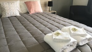 Una cama bien hecha con un edredón gris, dos almohadas y dos toallas dobladas sobre la cama.
