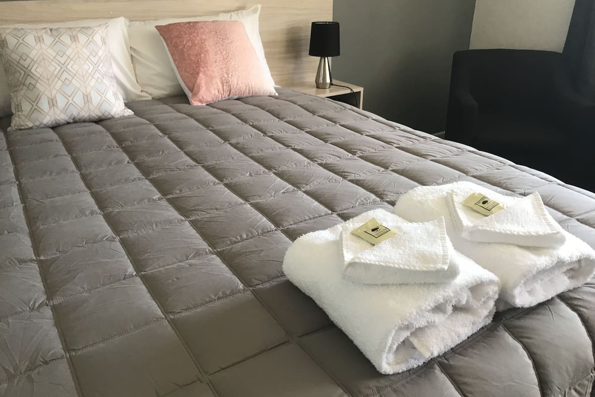 A neatly made bed with a grey quilt, two pillows, and two folded towels on the bed.