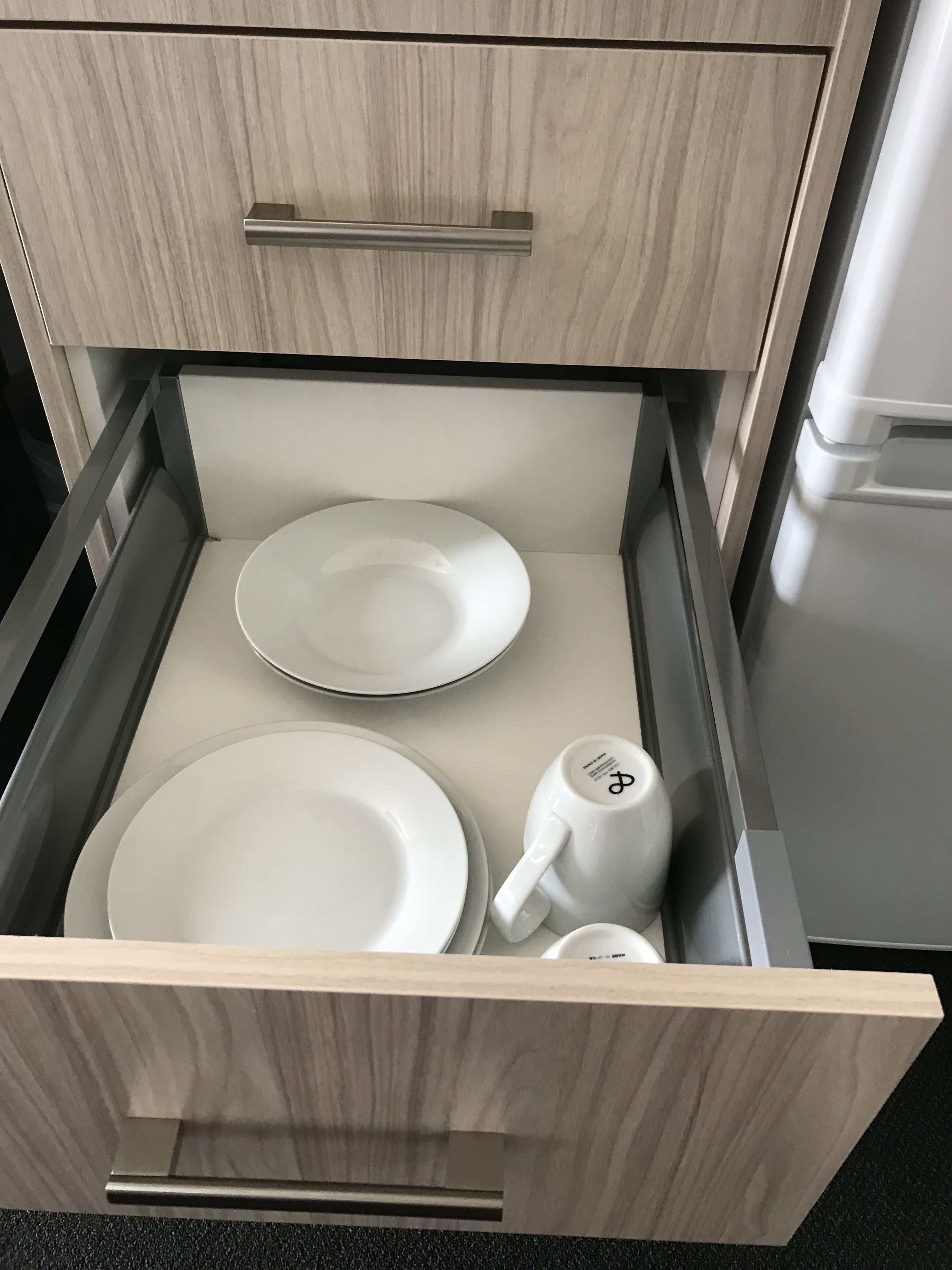 A drawer with white plates, a white mug, and a white bowl.