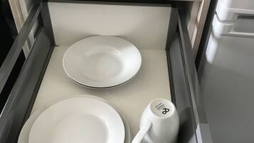 A drawer with white plates, a white mug, and a white bowl.