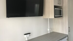 Una cocina moderna con un televisor de pantalla plana montado sobre un mueble de madera, un microondas integrado y una encimera gris.