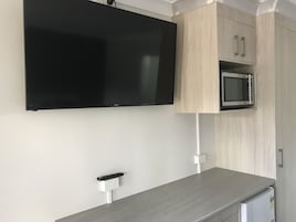 Cozinha moderna com televisão de tela plana fixada acima de um armário de madeira, micro-ondas embutido e bancada cinza.