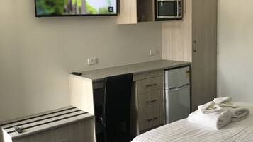 Ett modernt hotellrum med en säng, ett skrivbord med en mikrovågsugn, en TV och ett litet pentry.