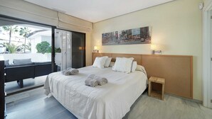 A hotel room with a large bed, a small wooden nightstand, a wall-mounted TV, and a sliding glass door leading to an outdoor area. - 1104 Charming Beachfront Apartment on Golden Beach (Marbella)