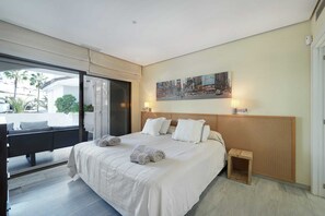 A hotel room with a large bed, a wooden headboard, a small bedside table, and a view of the outside through a sliding door. - 1104 Charming Beachfront Apartment on Golden Beach (Marbella)