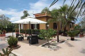 Un espace patio aménagé avec du mobilier d’extérieur, un parasol blanc et des plantes en pot.