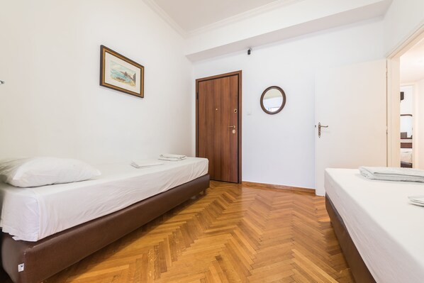 A bedroom with two beds, a wooden floor, a door, and a framed picture on the wall.