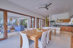 Una cocina moderna y espaciosa con una mesa de madera, sillas de mimbre blanco y una isla grande con taburetes de bar.