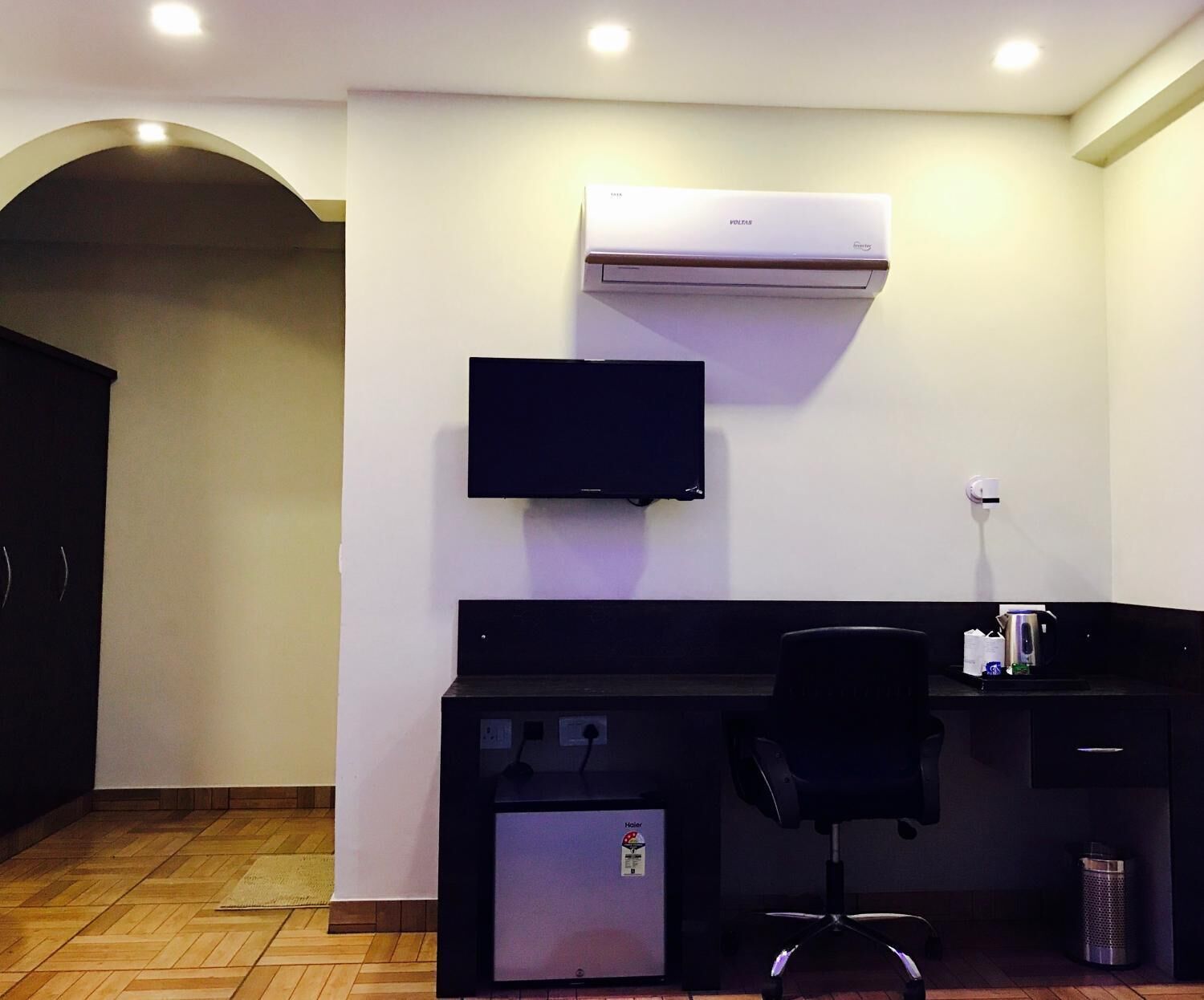 Une chambre d’hôtel équipée d’un bureau, d’une chaise, de la climatisation, d’une télévision et d’un petit réfrigérateur.